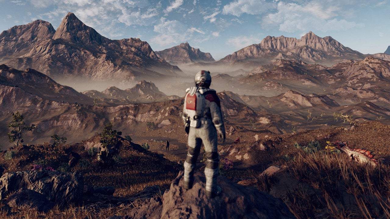 An in-game screenshot of Starfield, an astronaut standing on a rock looking out over a vast mountainous landscape with some creatures nearby.